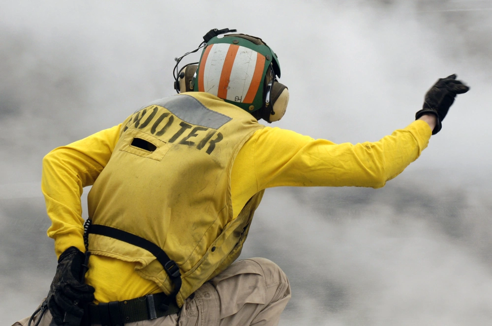 A catapult officer on USS Kitty Hawk gives a launch signal while steam rises around the flight deck in 2008.