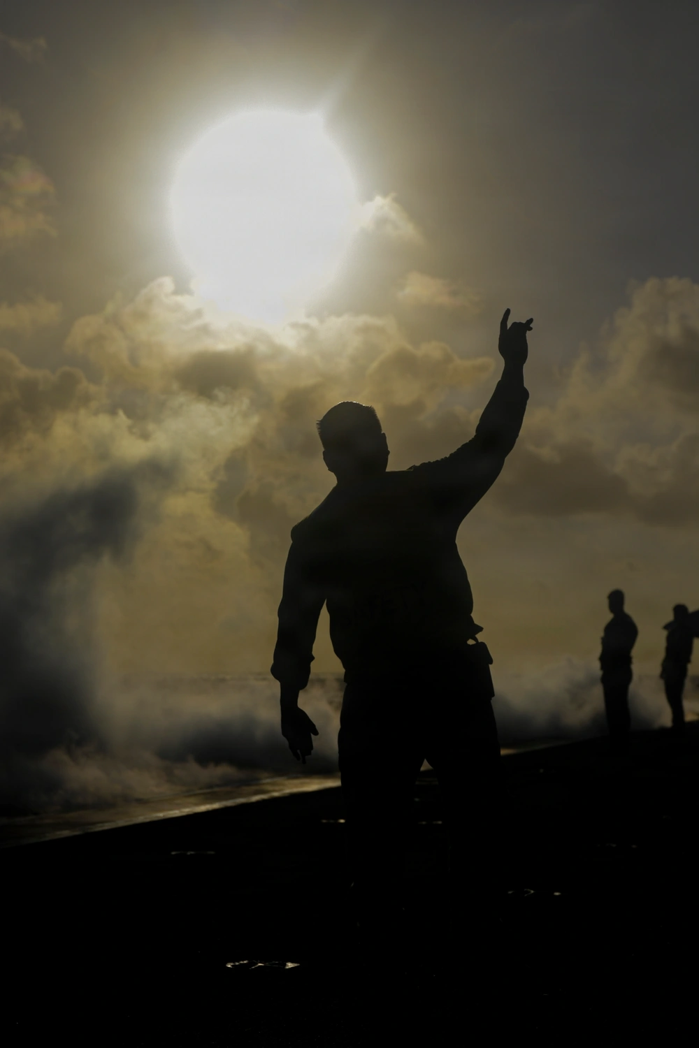 A silhouetted sailor signals during a steam-powered catapult test aboard USS Theodore Roosevelt at RIMPAC 2026, with steam across the deck.